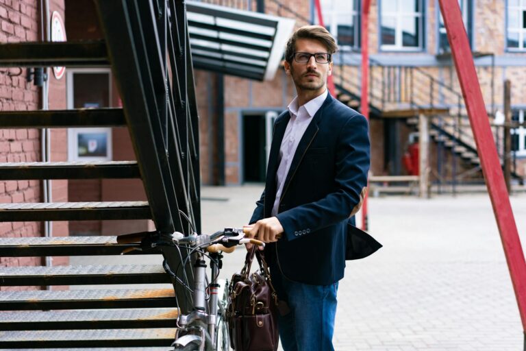 Elegant businessman with bicycle in cityscape, wearing a suit and carrying a briefcase.